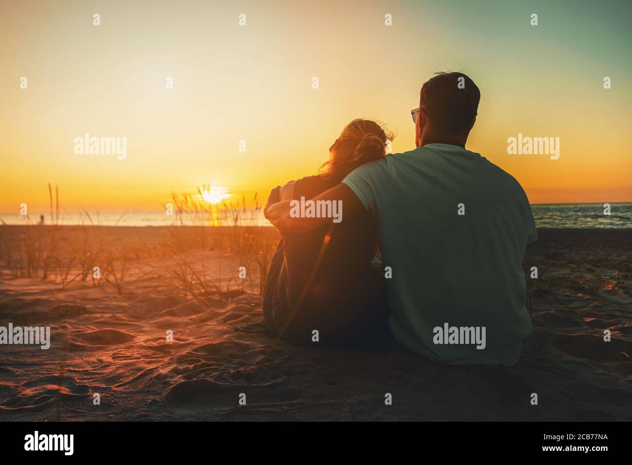 jóvenes amantes pareja sentado en la arena en la playa en la romántica puesta de sol de oro Foto de stock