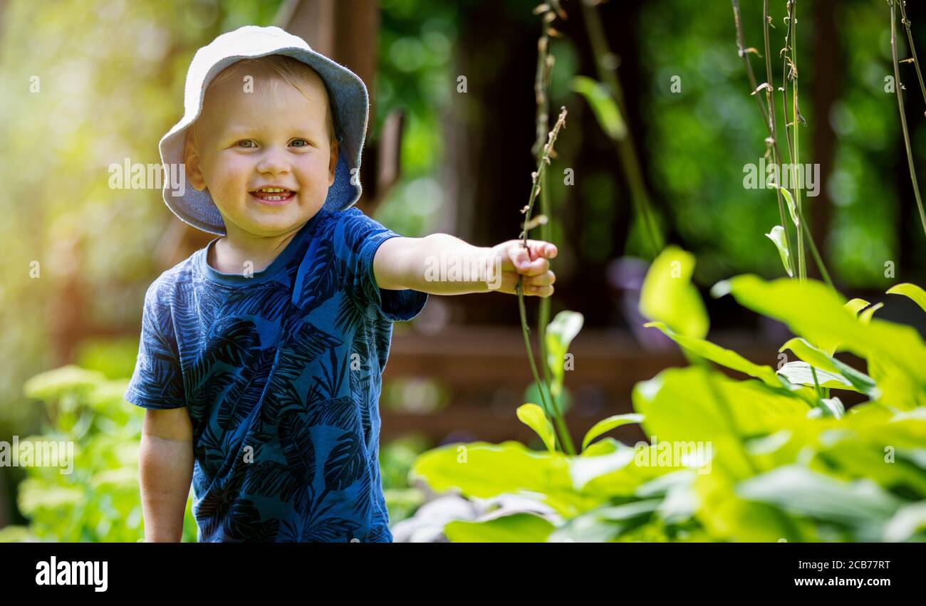 niño feliz y alegre que se divierte en el jardín. jugando con plantas. sonriendo y mirando con la cámara Foto de stock