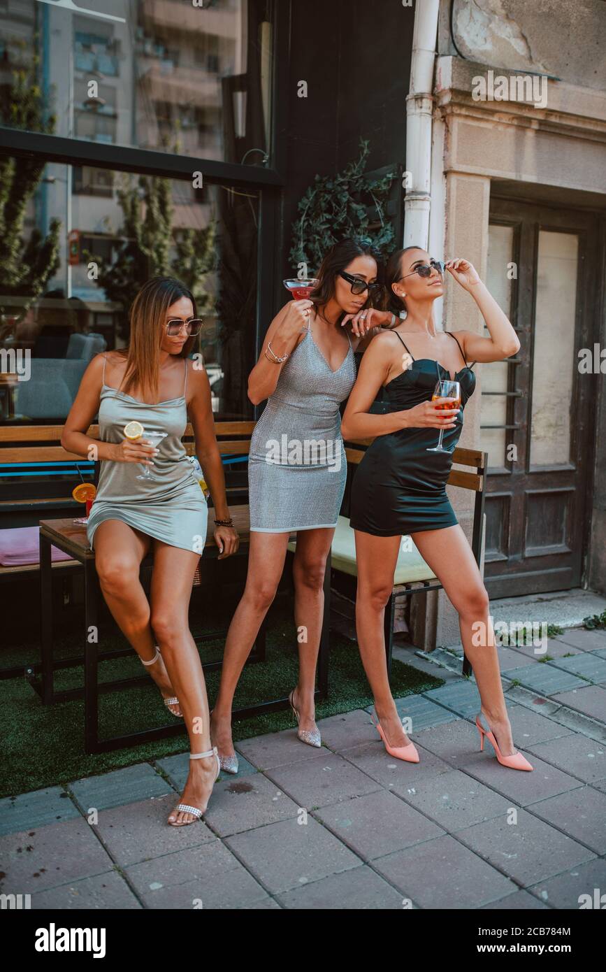 mujeres caucásicas atractivas en vestidos cortos y apretados beben cócteles  en un café-jardín. Chicas y fiestas Fotografía de stock - Alamy
