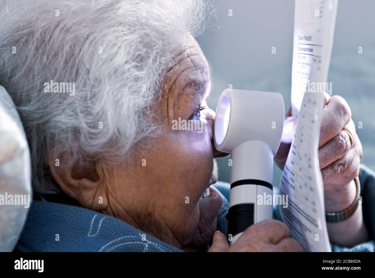 Anciana anciana anciana independiente anciana con degeneración macular leyendo un estado financiero en casa usando una poderosa lupa con luz función Foto de stock