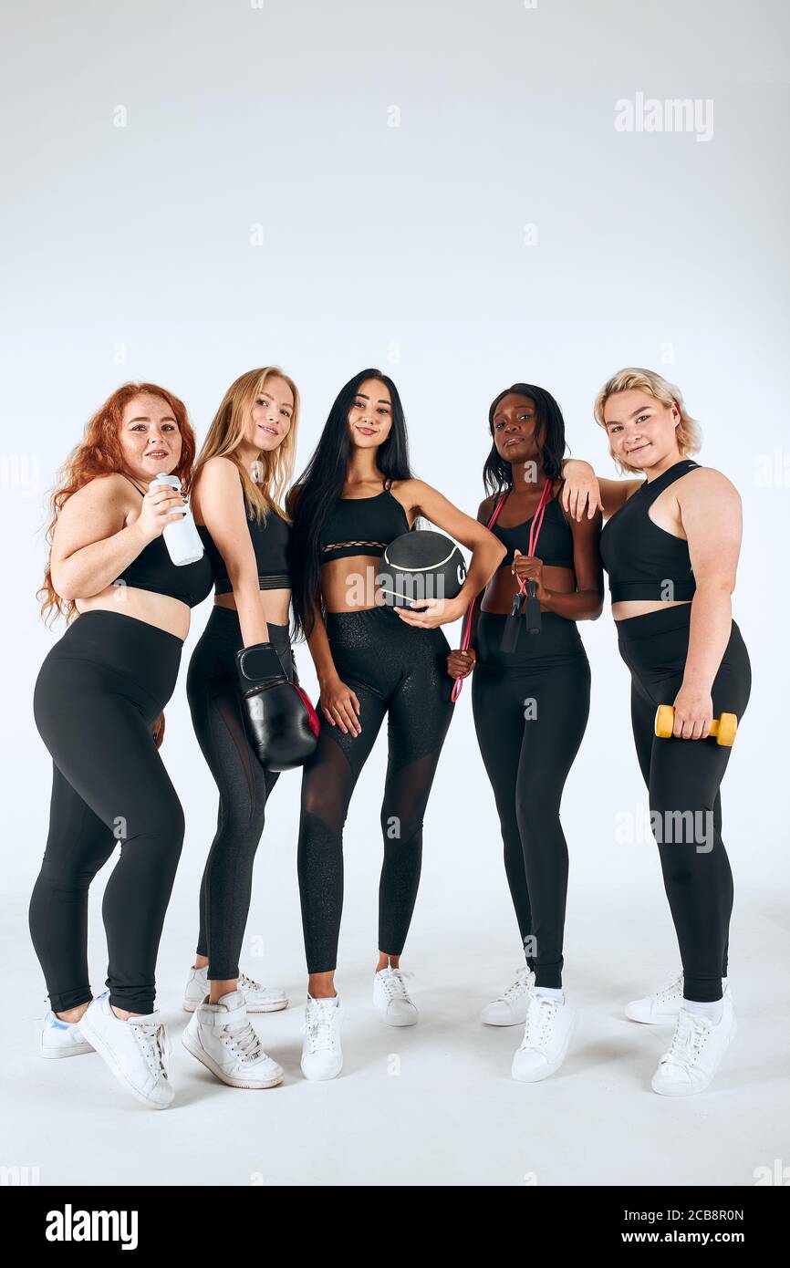 Cinco mujeres multiétnicas sonriendo con leggins deportivos y temas que  sostienen pelota de fitness, guantes de boxeo y otras cosas aisladas sobre  fondo blanco Fotografía de stock - Alamy