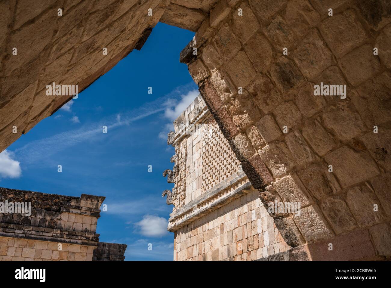 La vista a través de un arco en el Cuadrángulo de las aves en las ruinas de la ciudad maya de Uxmal en Yucatán, México. Las máscaras Chaac adornan la esquina de t Foto de stock