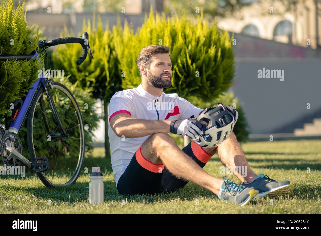 Ciclista masculino pensivo sobre la hierba descansando Foto de stock