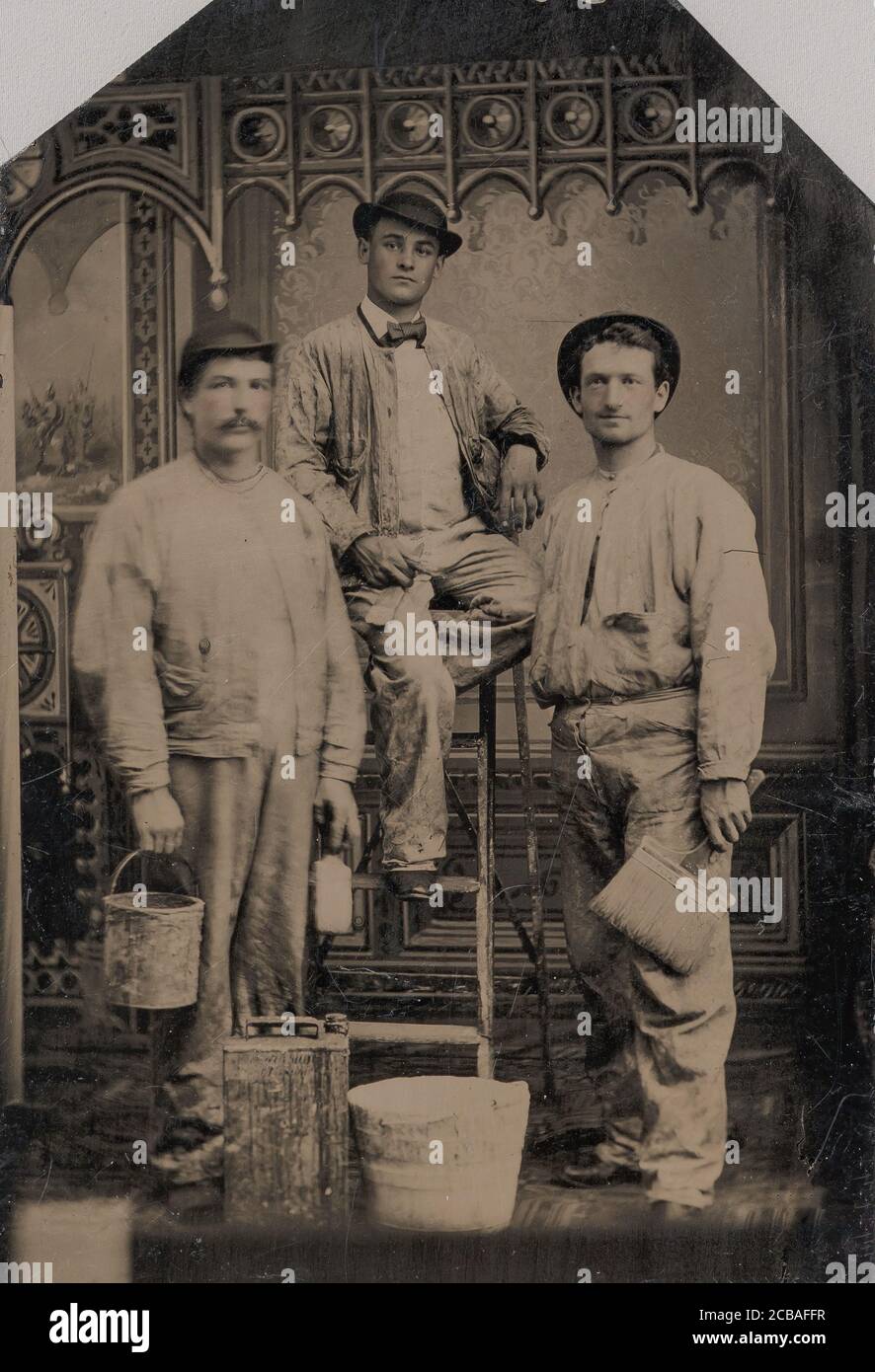 Tres pintores, dispuestos en y alrededor de una escalera, con cepillos, cubo, y la lata de pintura, 1870s-80s. Foto de stock