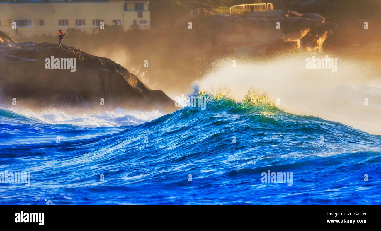 Acantilados de playa Bronte y fuertes olas del océano Pacífico en sol alrededor de solitarios pescadores en una roca de arenisca. Foto de stock