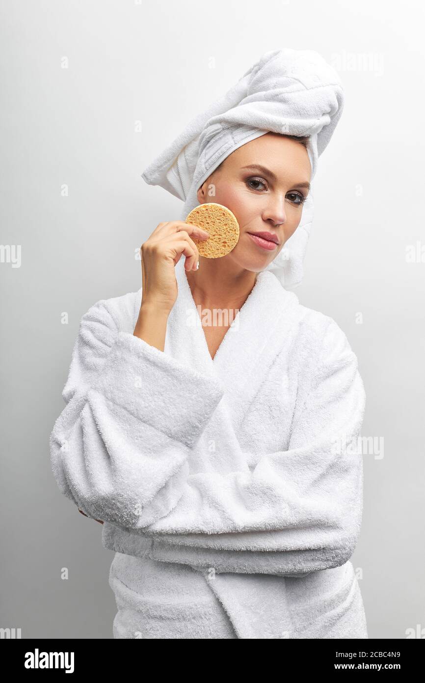 Hermosa señora en albornoz con toalla blanca en su cabeza una esponja gruesa beige para frotar en su mano derecha. Fondo blanco aislado Fotografía de stock - Alamy