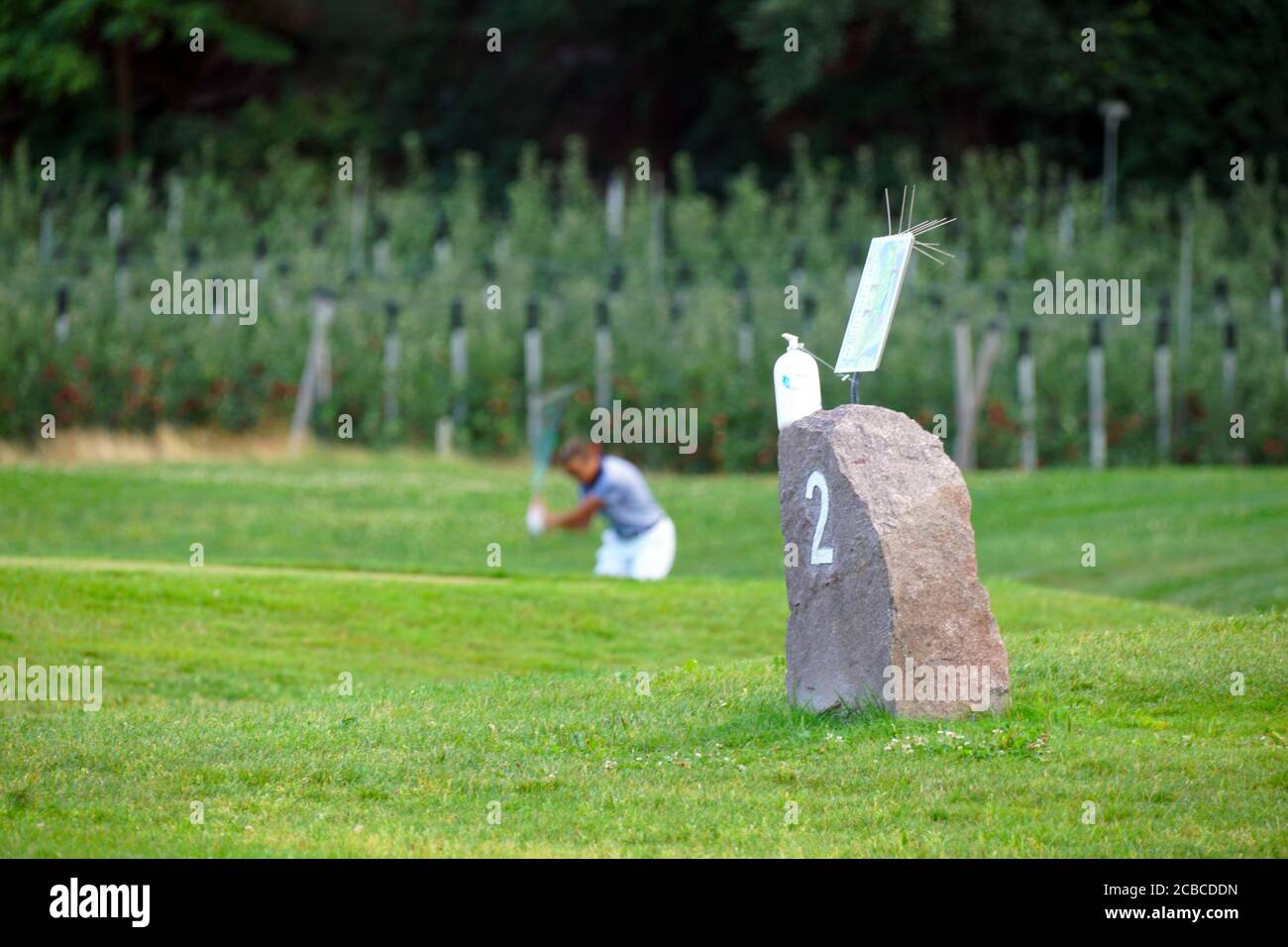 Golfista borroso en el fondo y una piedra con el número 2 en primer plano en el club de golf Blue Monster en el sur de Tirol, Italia. Foto de stock