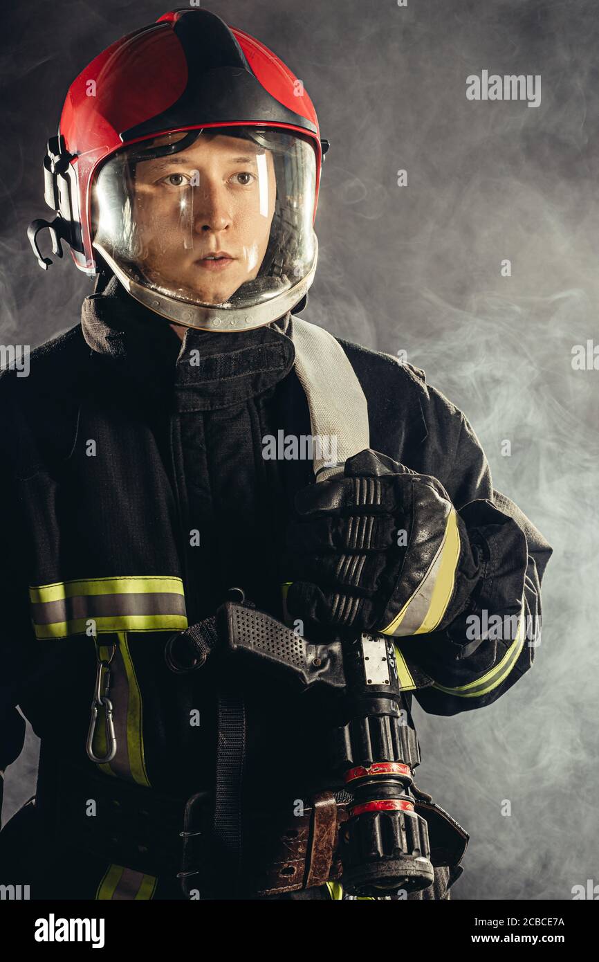 un joven bombero adulto que salva a la gente del fuego usando uniforme y  casco, sosteniendo el equipo de lucha contra incendios Fotografía de stock  - Alamy