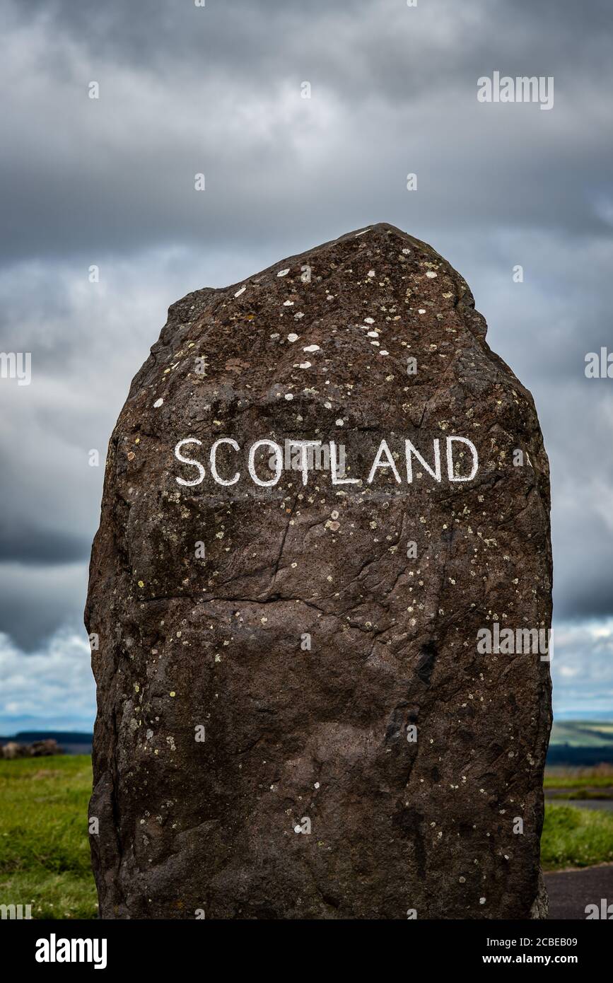 Una piedra de pie alta con la Marca grabada de la Palabra de Escocia La frontera entre Escocia e Inglaterra con nubes dramáticas La distancia Foto de stock