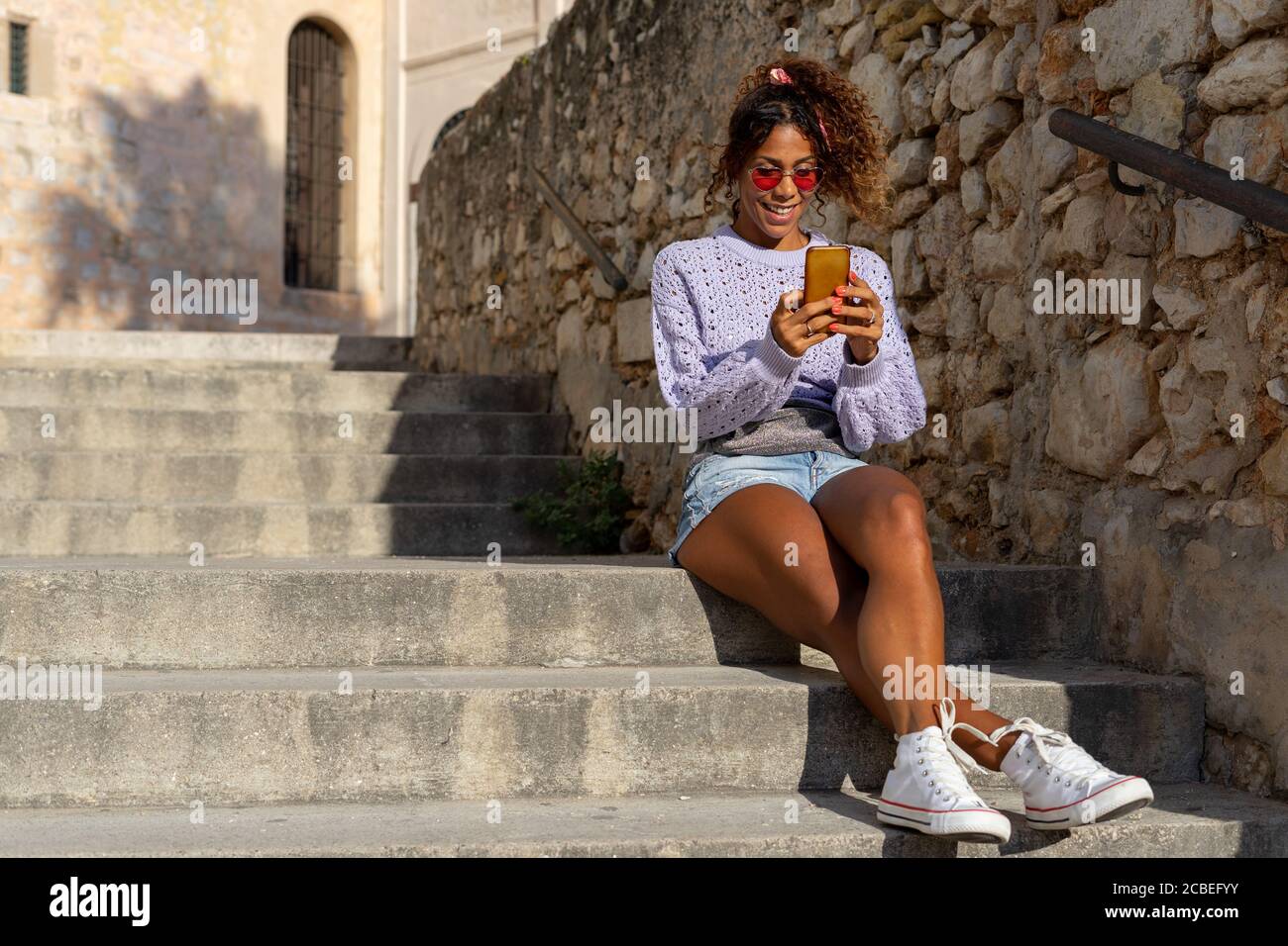 Retrato de una atractiva mujer negra joven tomando un selfie con su móvil. Hablando por teléfono sentado en las escaleras Foto de stock