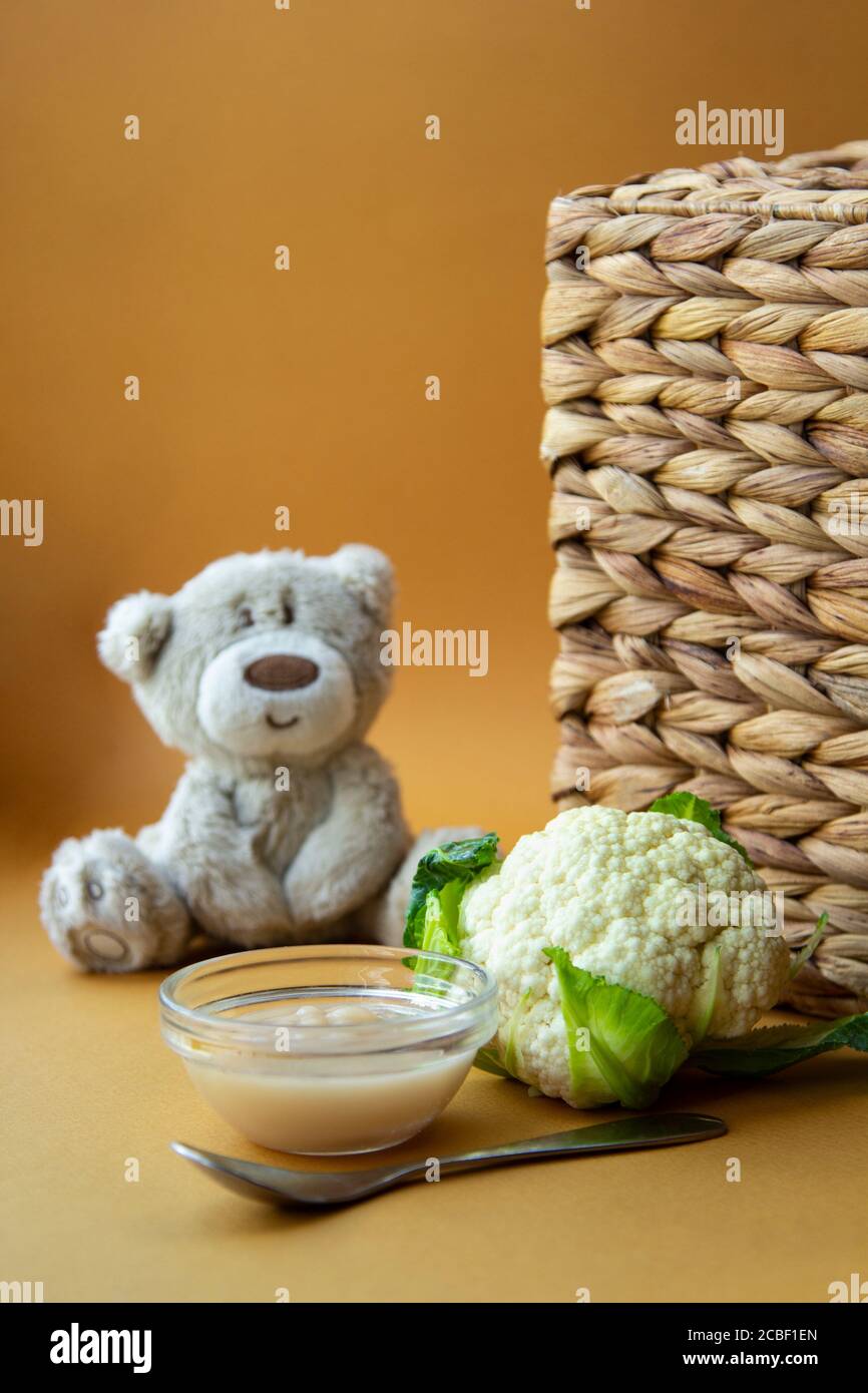 comida fresca para bebés en un tazón con cuchara y oso de peluche sobre  fondo marrón. Puré casero de coliflor Fotografía de stock - Alamy