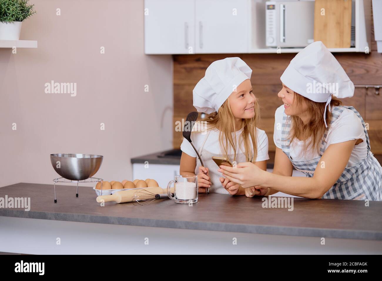 concepto de horneado, cocina. hermosa madre e hija se miran unos a otros con amor, yendo a hornear en la cocina Foto de stock