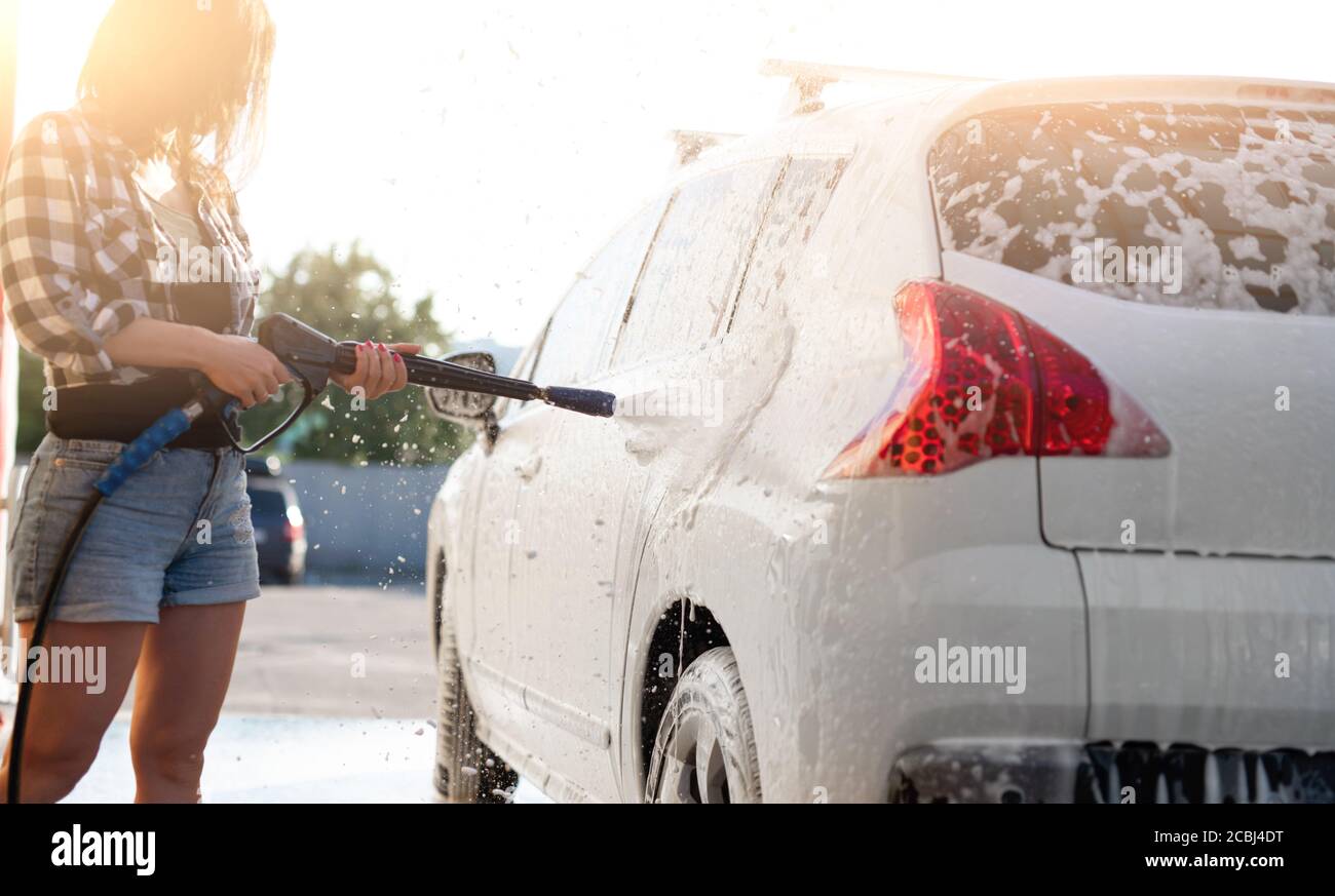 Un hombre apunta un pulverizador de espuma a un coche un coche en un lavado  de coches de autoservicio