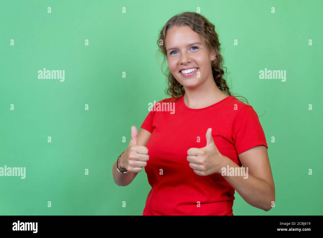 Mujer rubia con camisa roja mostrando el pulgar hacia arriba aislado fondo verde Foto de stock