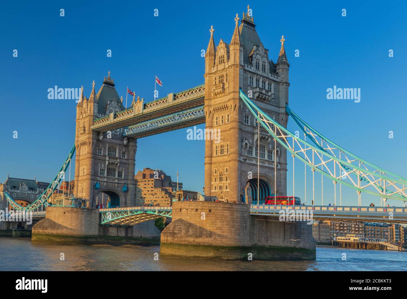 Inglaterra, Londres, Tower Bridge en la luz de la noche visto desde la orilla sur del río Támesis con un icónico autobús rojo de Londres cruzando el puente. Foto de stock