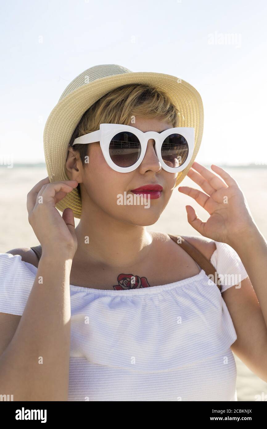 Un tiro vertical de una mujer caucásica con pelo corto y un tatuaje con  gafas de sol y un sombrero en el playa Fotografía de stock - Alamy