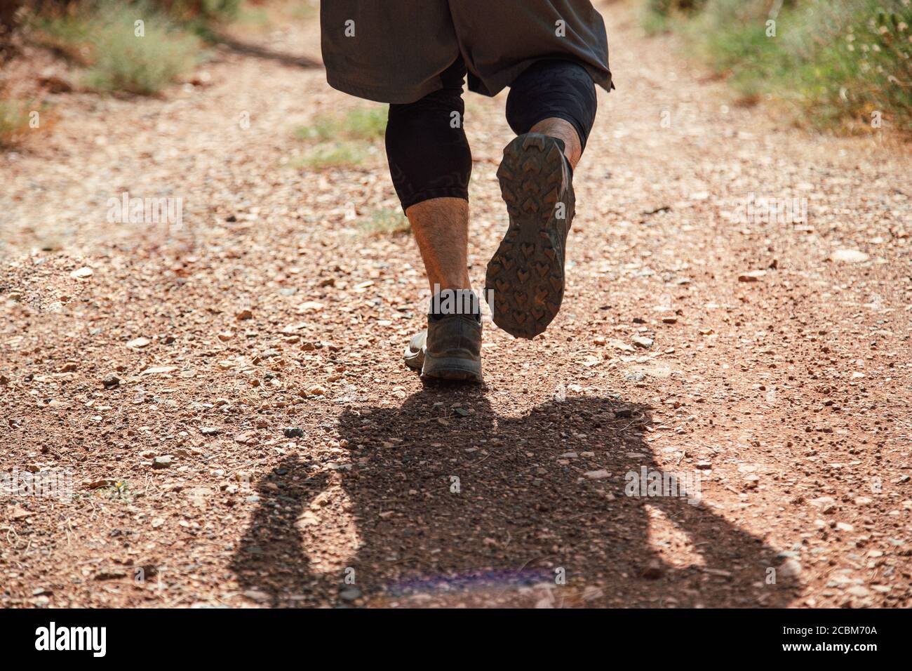 Atletas corredor corriendo por un sendero de montaña. Un hombre corre por las montañas entre las piedras. Vista desde atrás. Hombre en pantalones cortos y negro spandex Foto de stock