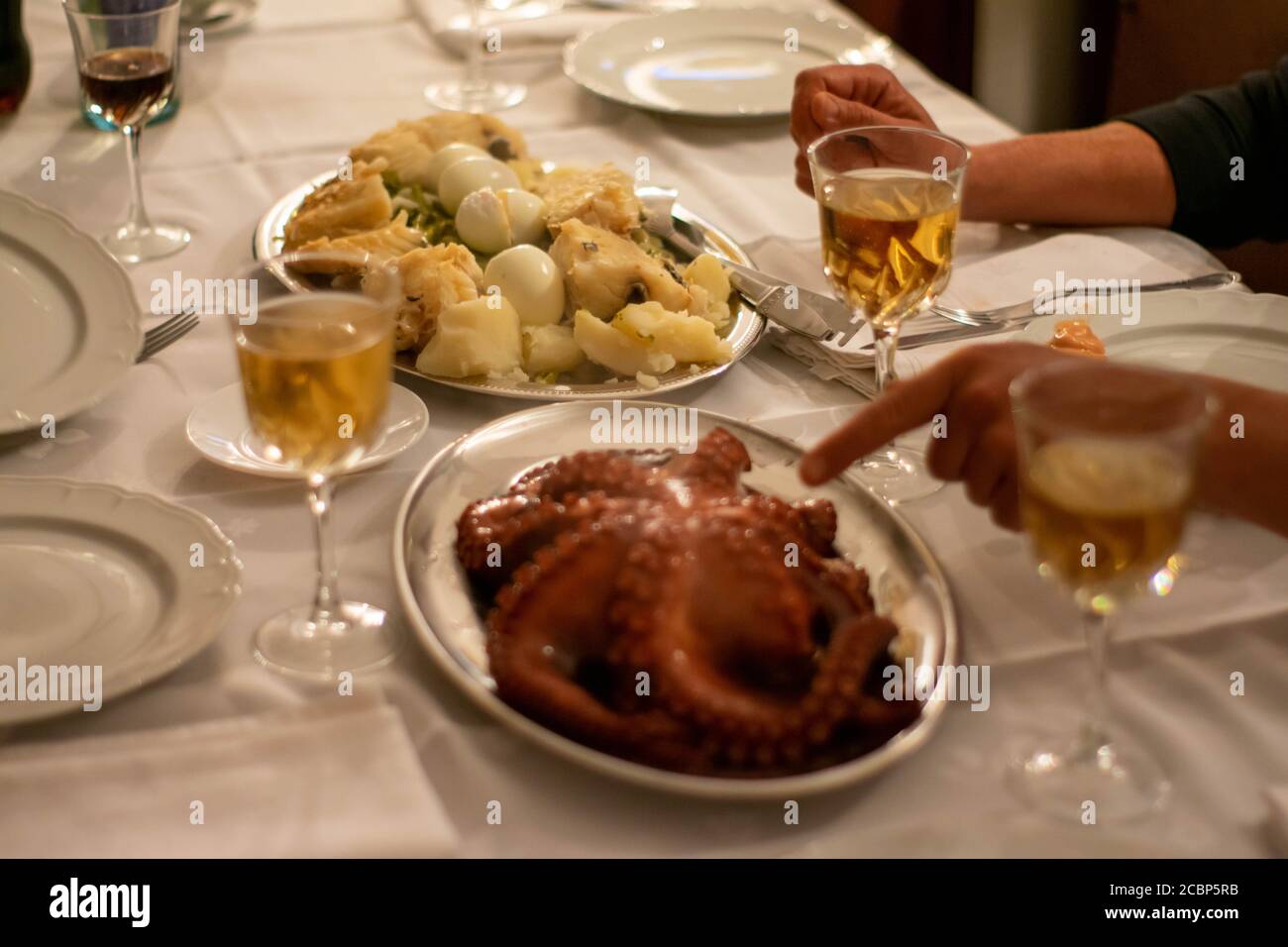 Persona apuntando a la comida en la mesa de Navidad con pulpo, huevos, patatas de bacalao y vino blanco. Mesa de comida tradicional portuguesa para Navidad. Foto de stock