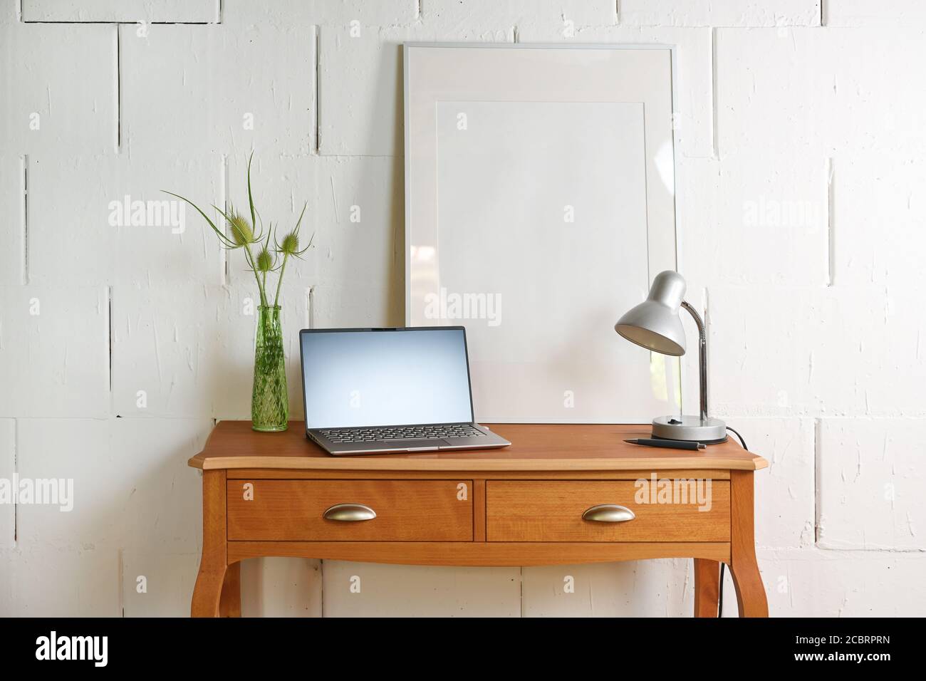 Pequeña mesa vintage de madera rojiza con ordenador portátil, lámpara de  escritorio y un marco de fotos delante de una pared blanca cruda, un pequeño  lugar de oficina en el hogar en