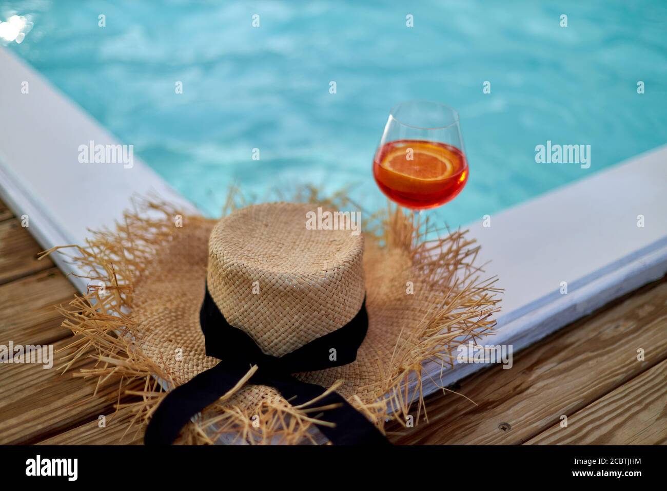 Cóctel de vidrio frente a un sombrero de paja situado en un paseo marítimo  de madera junto al mar. Concepto de vacaciones de verano con accesorios de  playa Fotografía de stock -