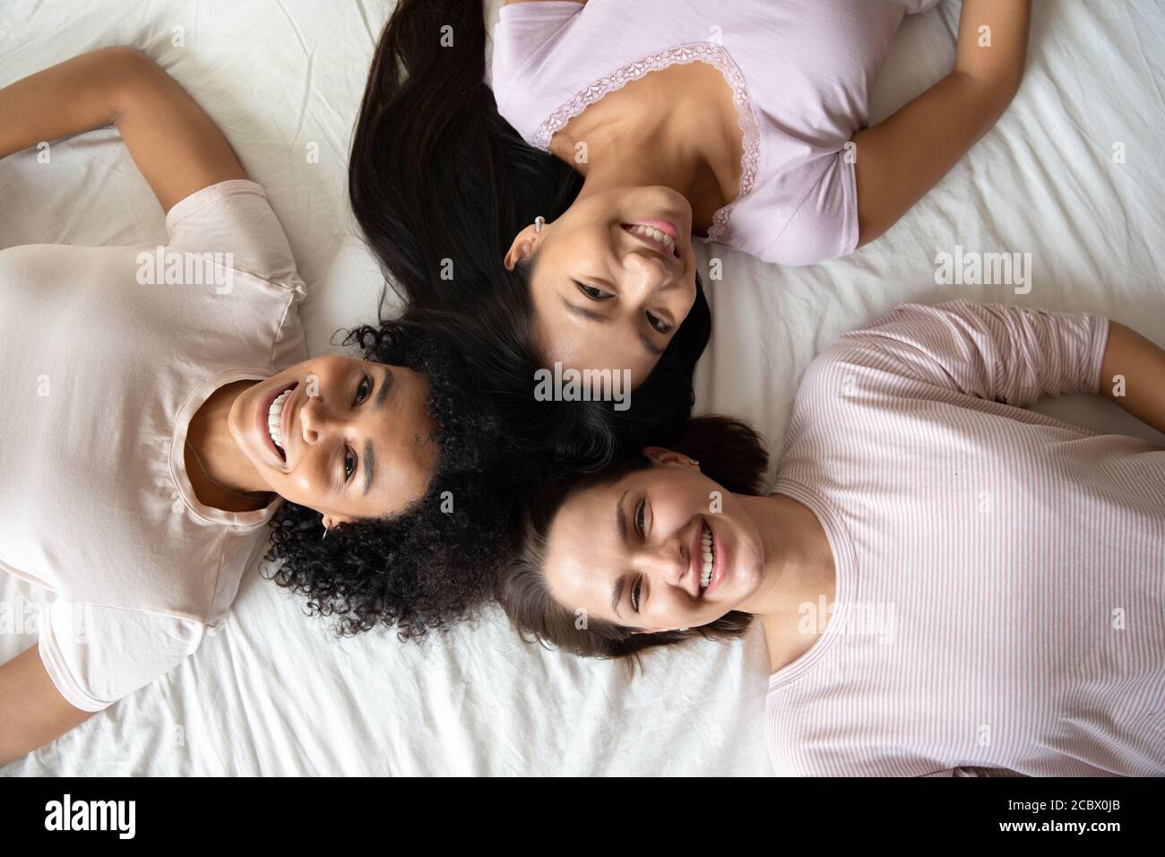 Tres mejores amigas diversas sonriendo tumbadas en la vista de la cama