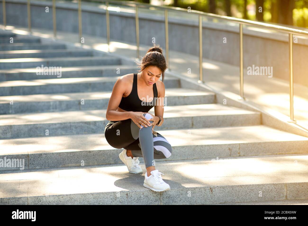 Chica negra con ropa deportiva sentada en las escaleras, masajeando la  rodilla Fotografía de stock - Alamy