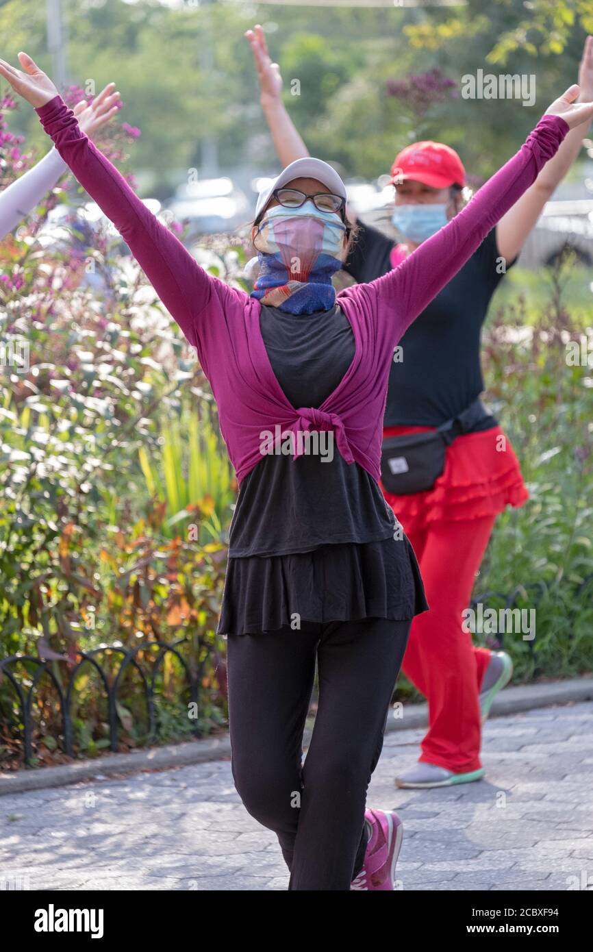 Un instructor de clase de danza chino-americana con una máscara quirúrgica y una bufanda de cara ornamentada. En una clase en un parque en Flushing, Queens, Nueva York. Foto de stock