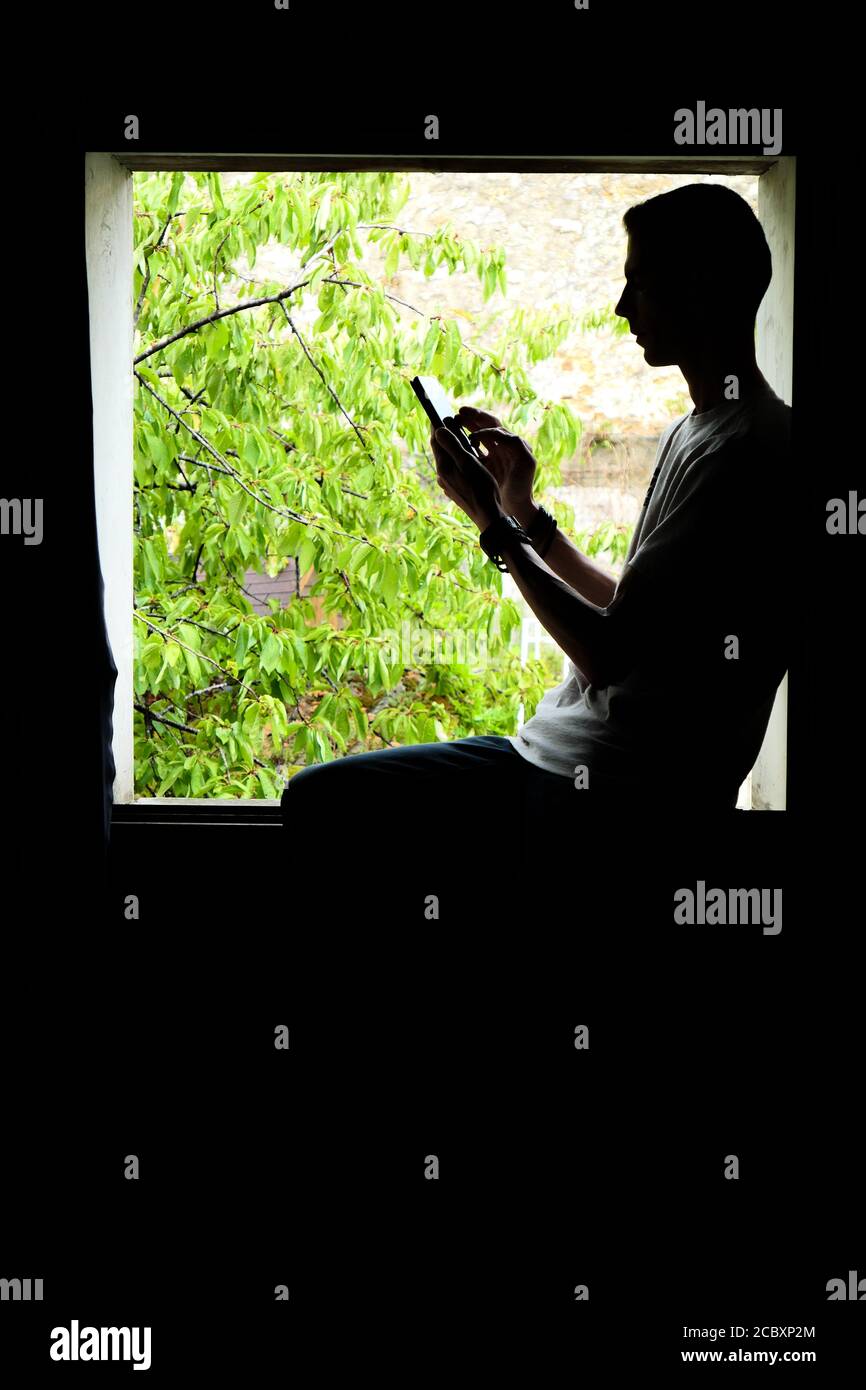 Persona que utiliza tecnología. Silueta de un hombre en el interior de una ventana, con un smartphone en sus manos. Foto de stock