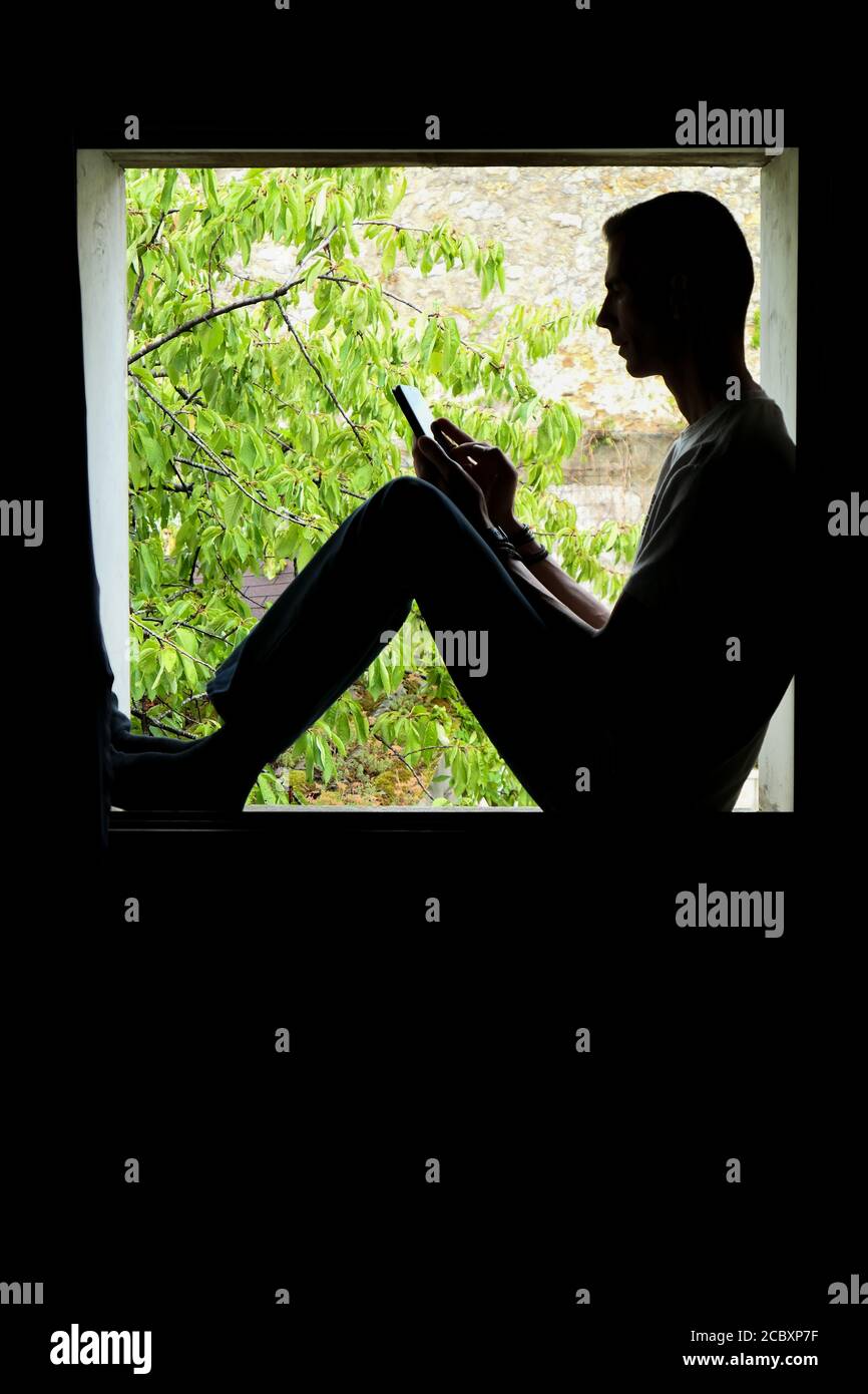 Persona que utiliza tecnología. Silueta de un hombre en el interior de una ventana, con un smartphone en sus manos. Foto de stock