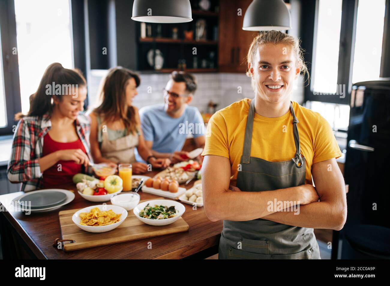 Grupo de amigos felices riendo y hablando mientras preparan las comidas en la cocina Foto de stock