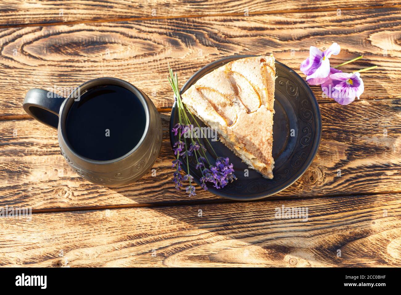 Pedazo de pastel de manzana con taza de té de cerámica hecha a mano sobre mesa rústica de madera Foto de stock