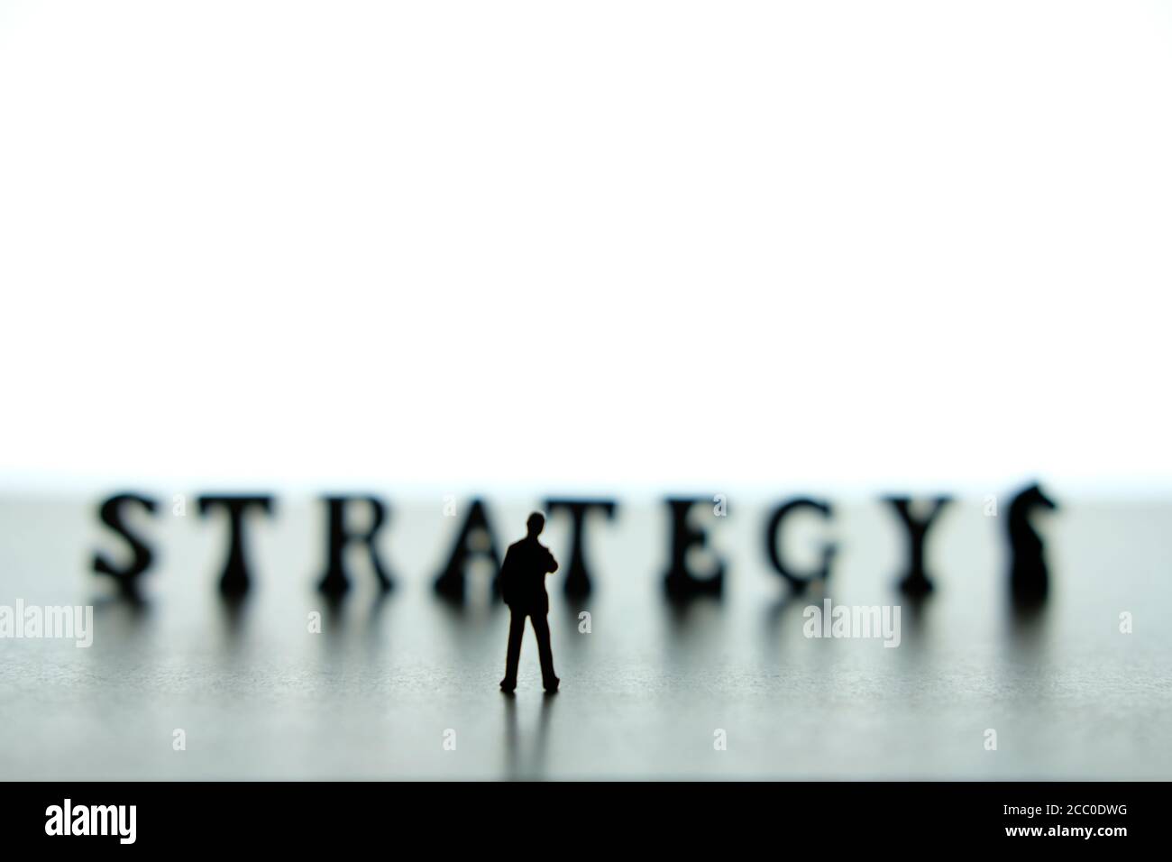 Silueta de hombres de negocios en miniatura de pie y pensando frente a rompecabezas de bloques de palabras de estrategia Foto de stock