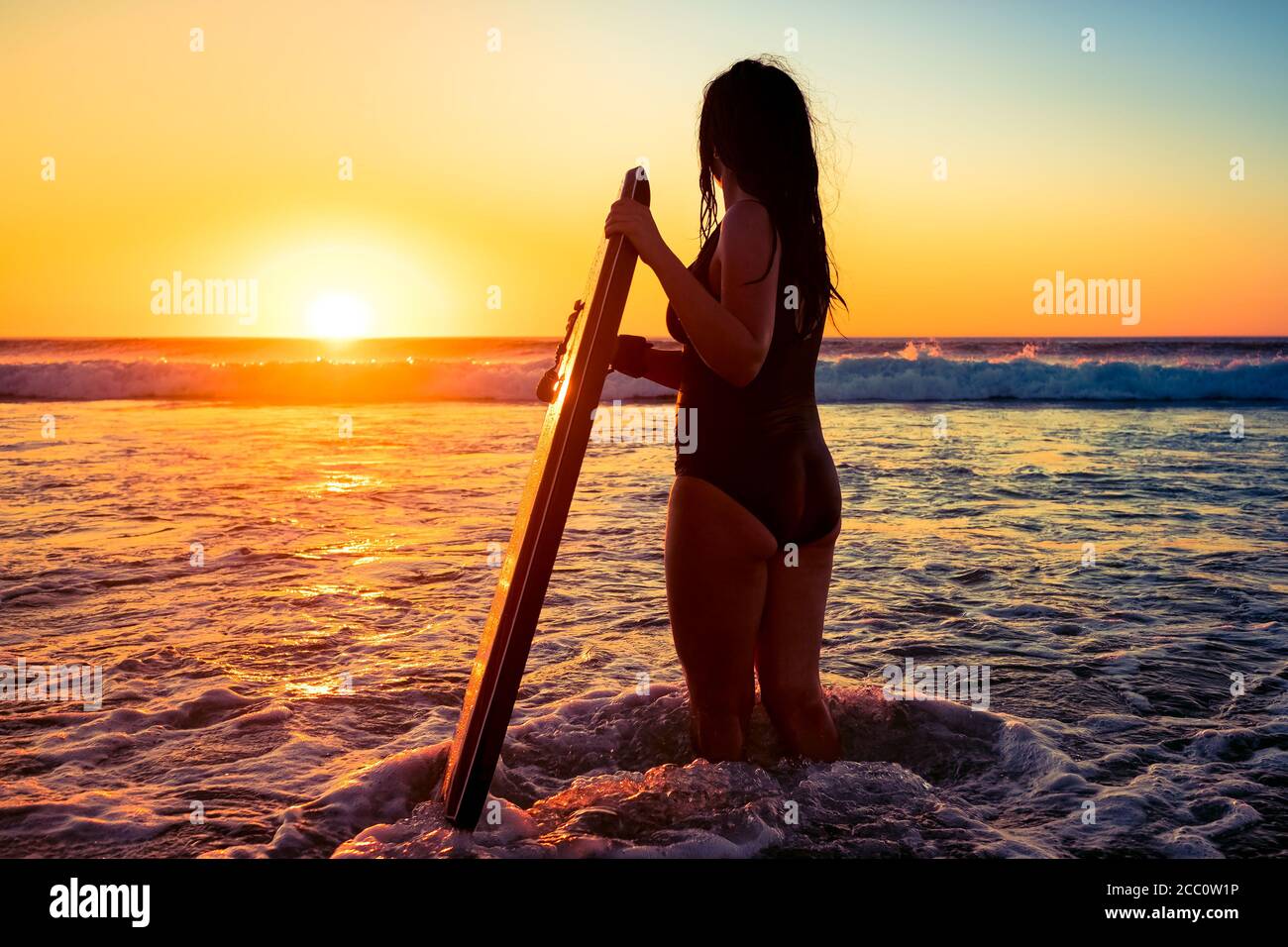 Mujer con bodyboard que captura olas rompientes al atardecer, Moana Beach, Australia del Sur Foto de stock
