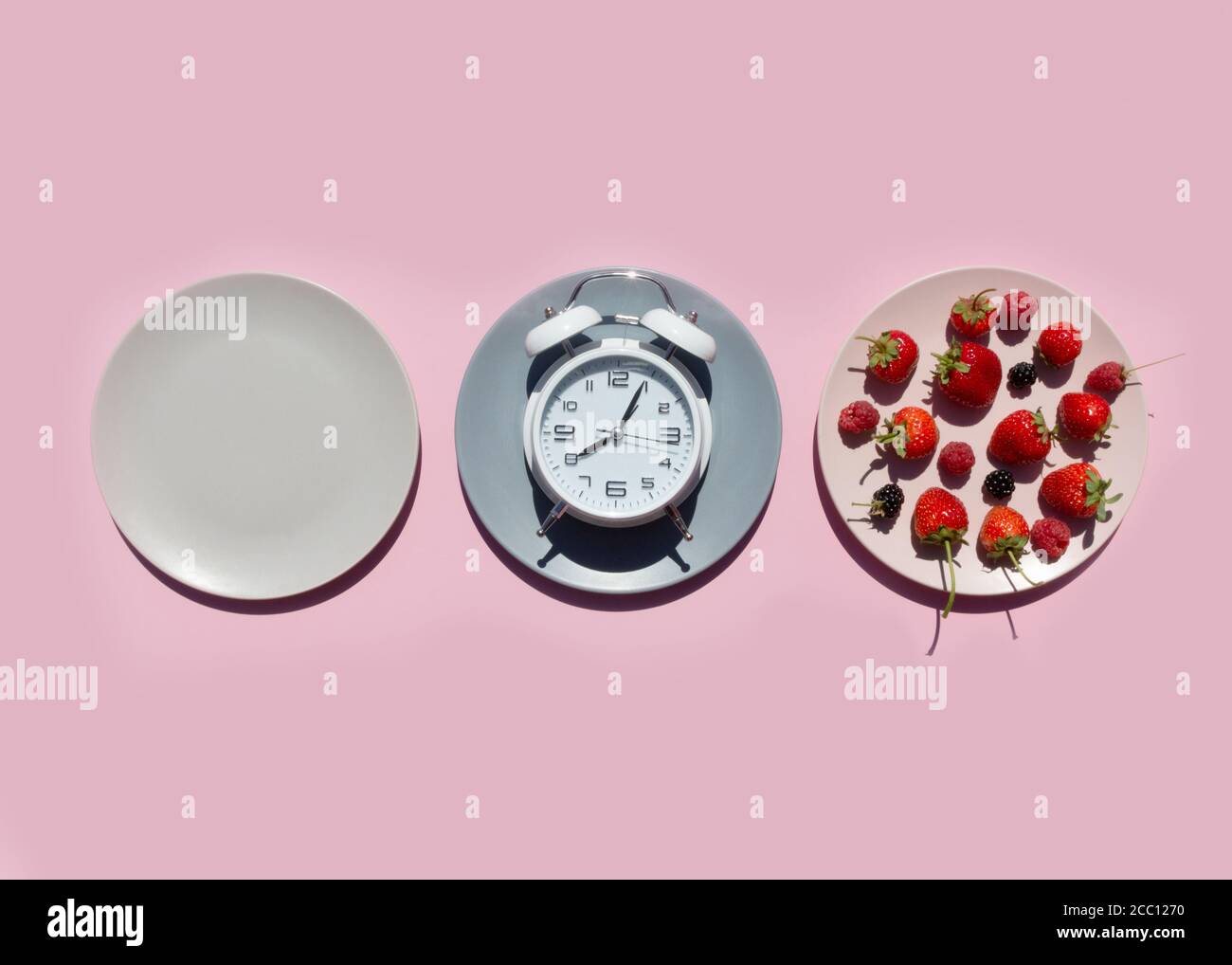 Concepto de ayuno intermitente con platos vacíos de colores. En el plato están las bayas, fresas, frambuesas, moras.tiempo para perder peso, comiendo Foto de stock