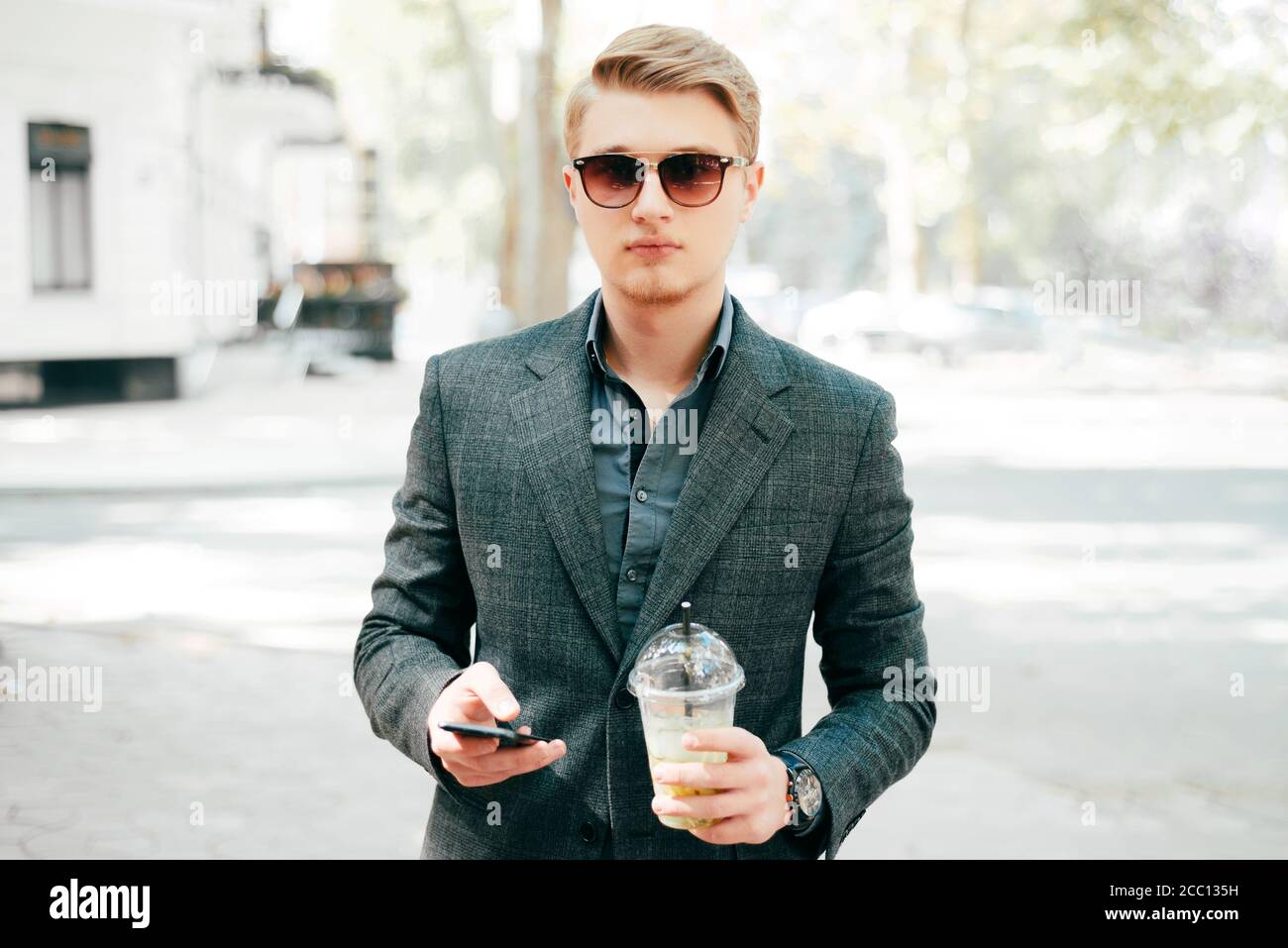 Retrato de un hombre guapo en traje bebiendo limonada y sosteniendo un  smartphone Fotografía de stock - Alamy