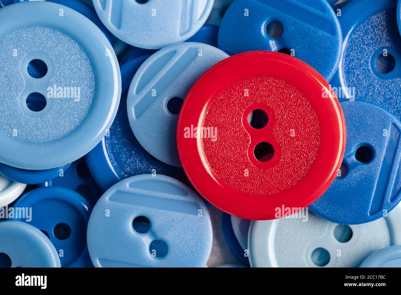 Botón rojo sobre fondo de botones de plástico azul. Este archivo se limpia y se vuelve a archivar. Foto de stock