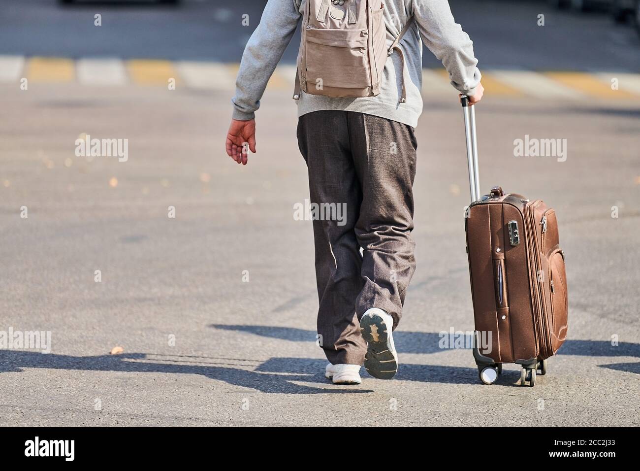 Hombre viejo con maleta sobre ruedas. Varón con bolsa de equipaje bajando  la calle desde el aeropuerto. Regreso a casa después del viaje. Efecto jet  lag. Vista posterior Fotografía de stock -