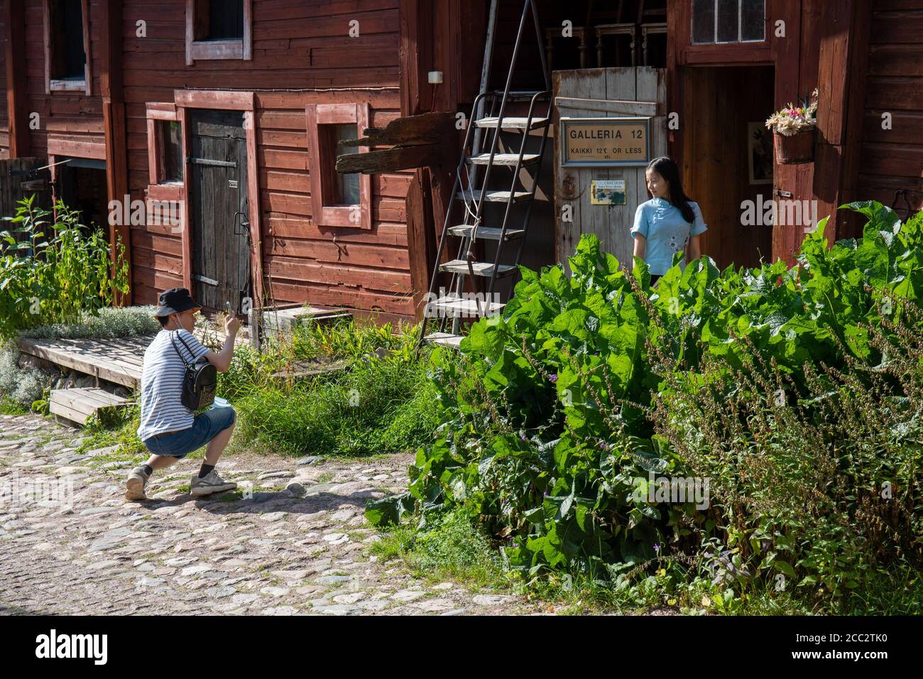Turistas tomando fotos de viaje contra el edificio de almacenamiento de madera de ocre rojo en el casco antiguo de Porvoo, Finlandia Foto de stock