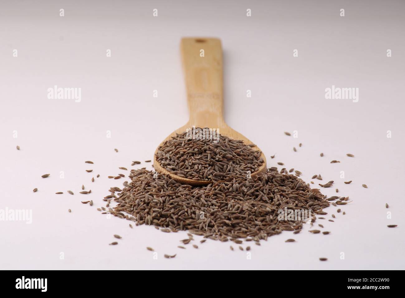 Cuchara de madera llena de semillas de comino aisladas sobre el fondo blanco. Foto de stock