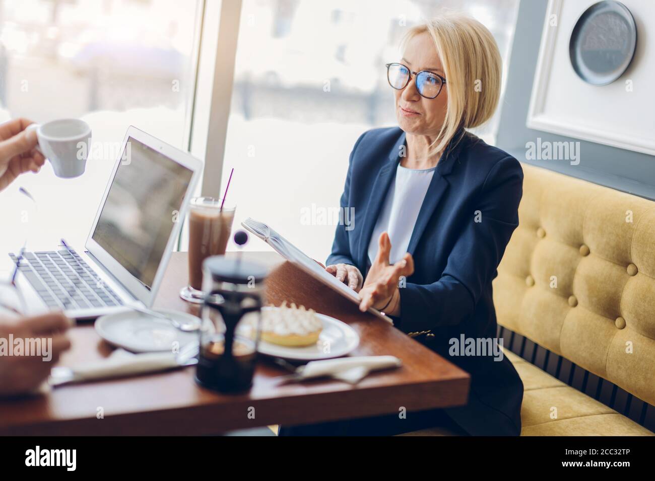 mujer de negocios de éxito compartiendo con sus secretos de negocio. de cerca vista lateral foto. mujer de edad encantadora hablando con un cliente en el café Foto de stock