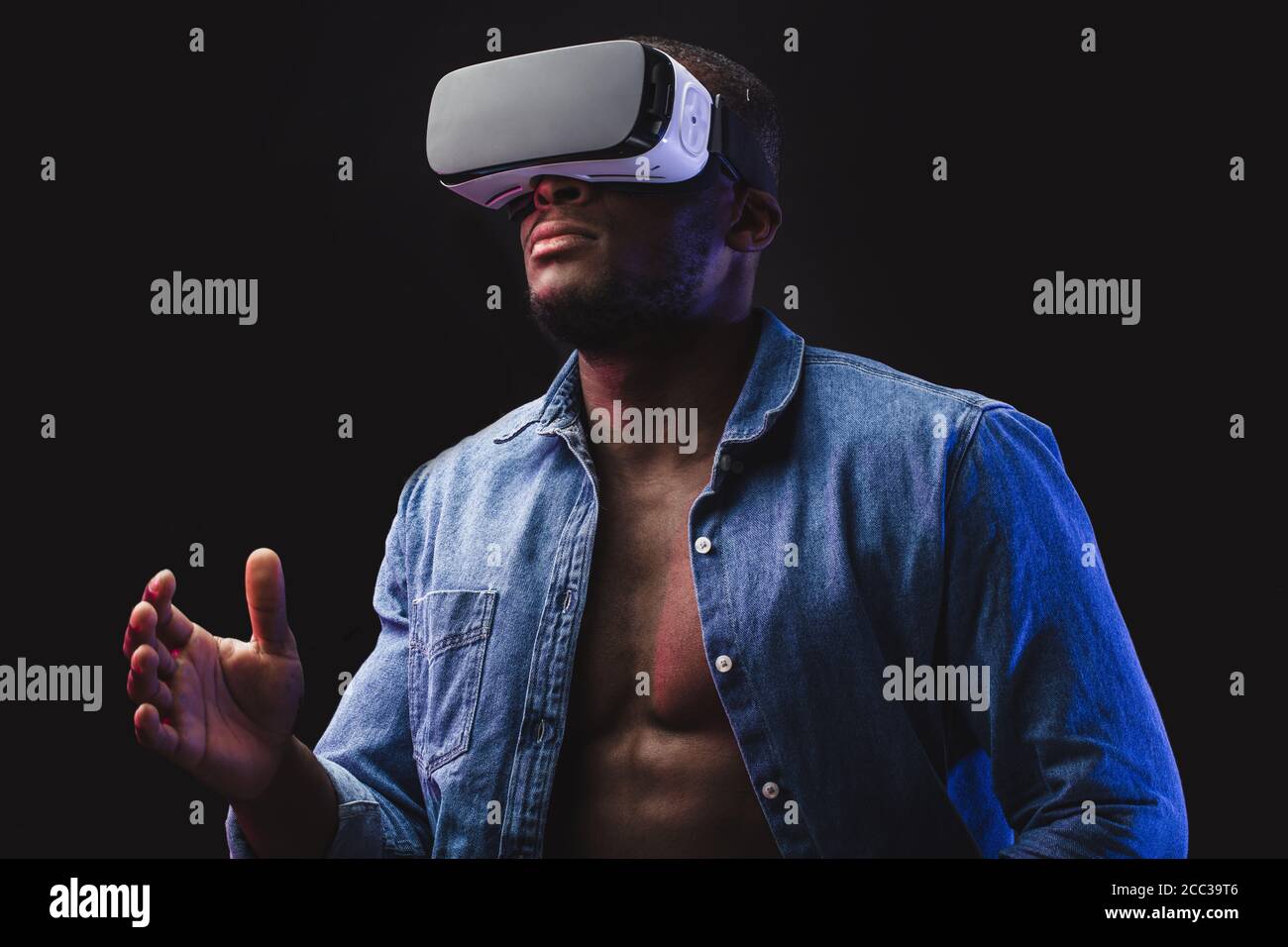 Concepto de juego. Hombre informal africano con auriculares VR móviles disfrutando de la nueva realidad en la habitación oscura Foto de stock