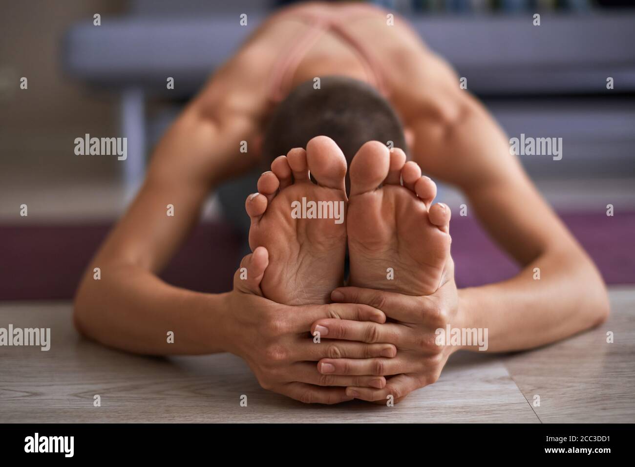 Cerca de los pies femeninos, mientras que el estiramiento de la alfombrilla. Estiramiento sentado en ejercicio de inclinación hacia adelante, paschimottanasana pose. Mujer vestida en ropa deportiva Foto de stock