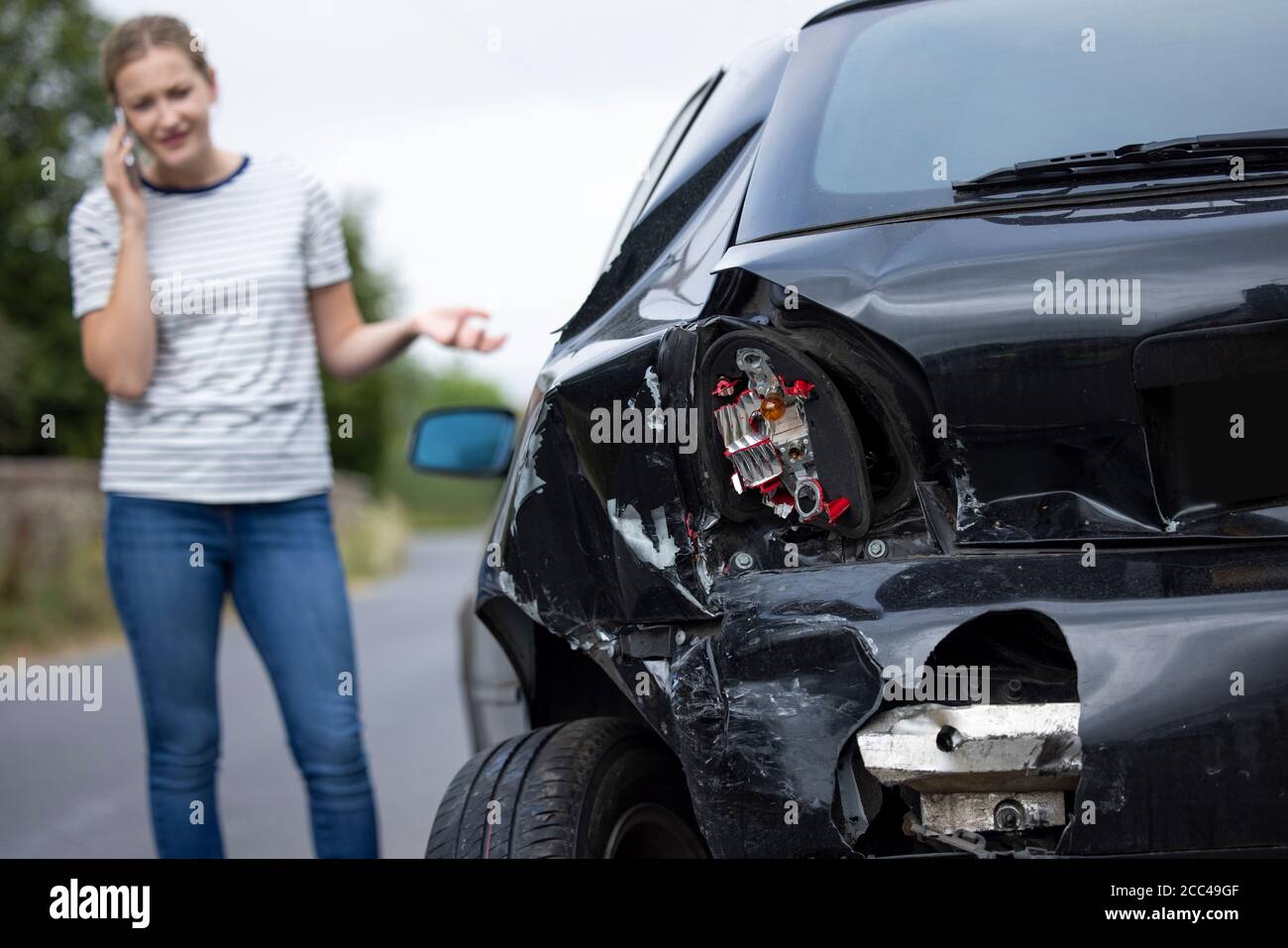 Conductor femenino infeliz con coche dañado después de accidente llamando al seguro Empresa en el teléfono móvil Foto de stock