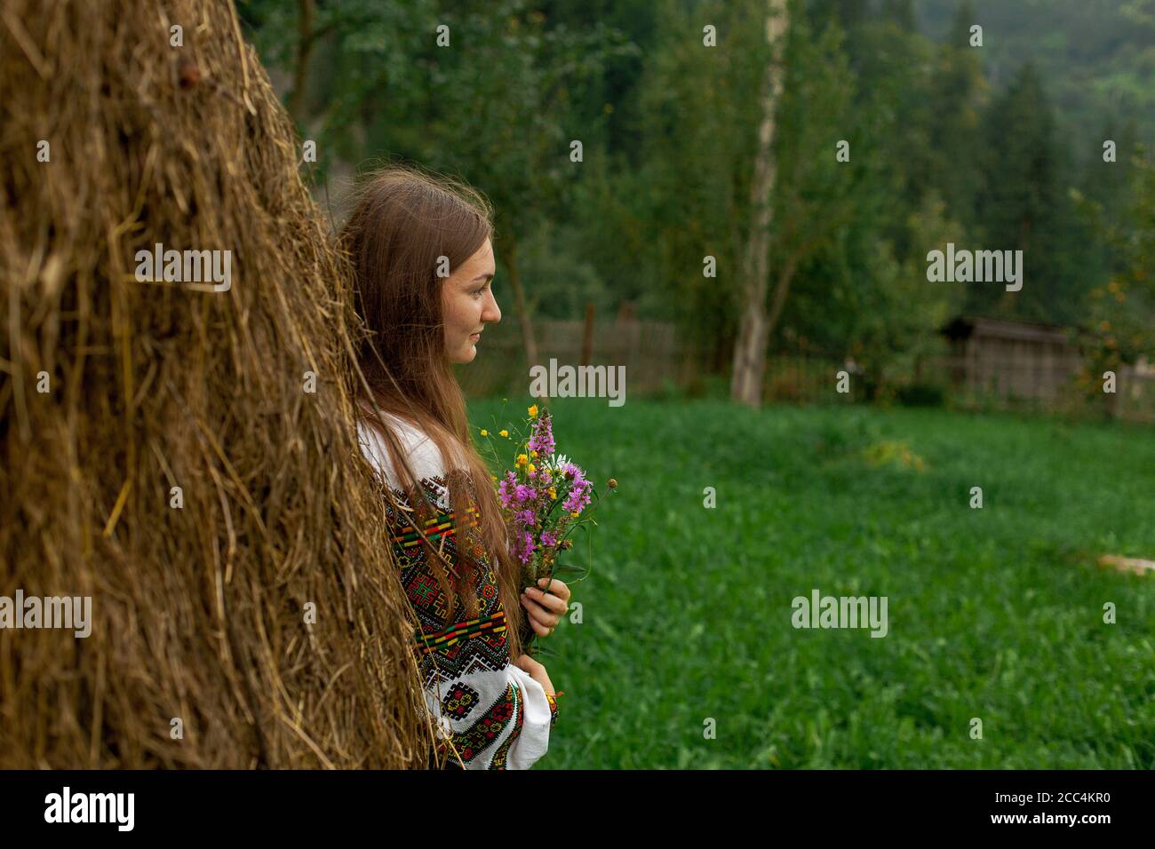 chica con pelo suelto con un ramo de flores silvestres se pone de pie por un pajar Foto de stock