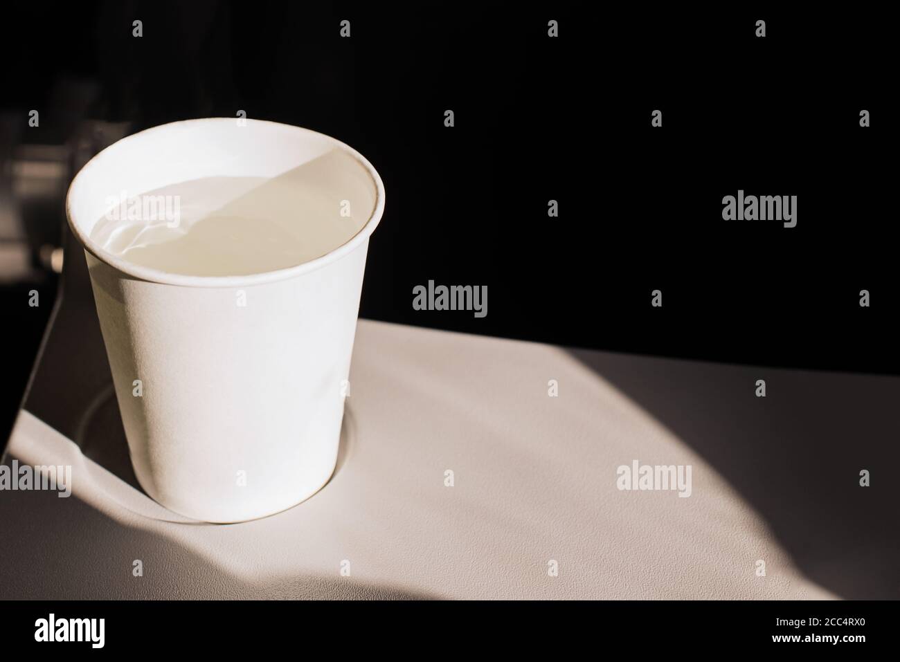 Taza de papel blanco de agua y auriculares en una mesa plegable en un avión.  Bebidas en el avión. Deshidratación en vuelo. Hidratación de la piel  Fotografía de stock - Alamy
