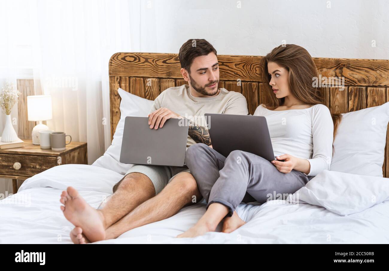Ocio nocturno moderno. El chico y la chica se acuesta en la cama con ordenadores portátiles y hablando Foto de stock