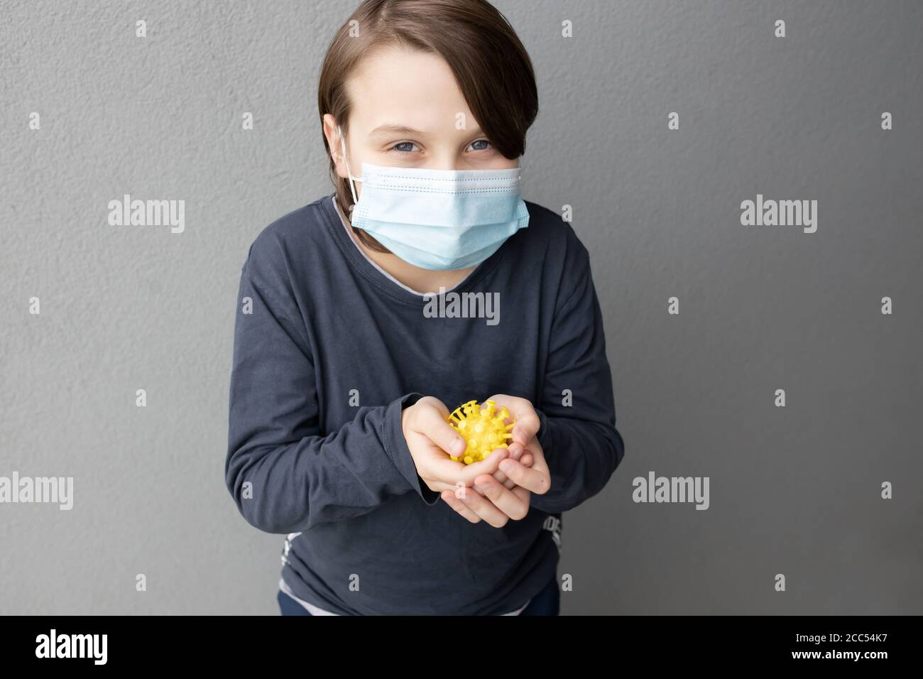 Niño caucásico joven con una máscara quirúrgica azul y sujeción Un modelo de virus de corona durante la pandemia de COVID-19 Foto de stock