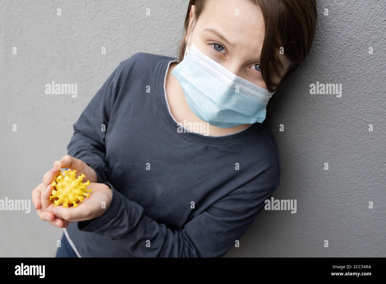 Niño caucásico joven con una máscara quirúrgica azul y sujeción Un modelo de virus de corona durante la pandemia de COVID-19 Foto de stock