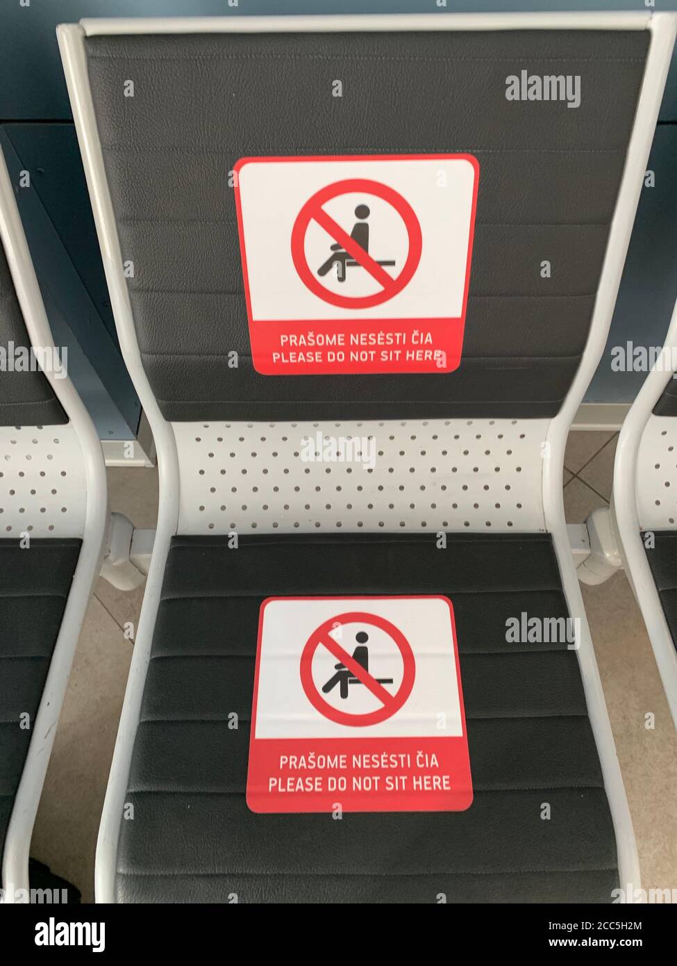 Por favor, no se siente aquí letrero en banco en el aeropuerto de Vilnius. Los pasajeros tienen que mantener 1-2 metros de distancia social para protegerse de la propagación del virus de la corona. Foto de stock