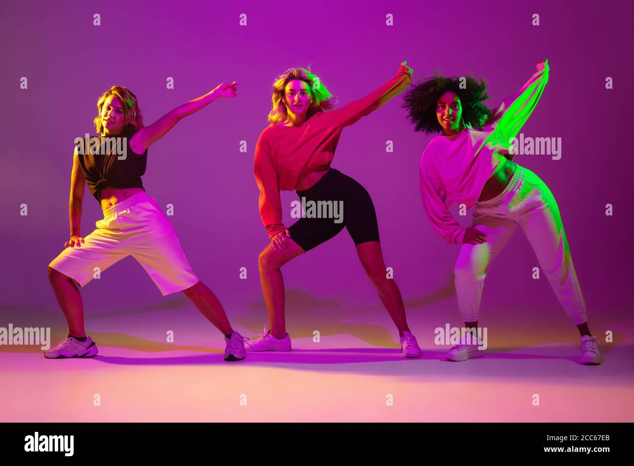 Flexible. Chicas deportivas bailando hip-hop con ropa elegante sobre fondo  púrpura-rosa en la sala de baile con luz de neón verde. Cultura juvenil,  movimiento, estilo y moda, acción. Retrato de moda Fotografía